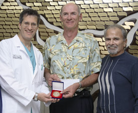 Craig Mueller, center, and Lowell “Blackie” Ballas present Nicholas Namias, M.D. with the $15,000 donation from the state-wide Florida Firefighter Games.